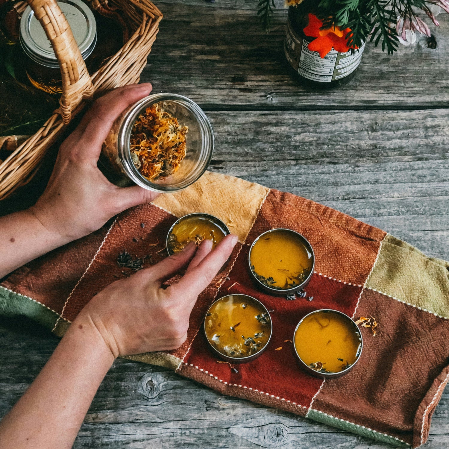 Person holding a jar over a woven mat with small containers on a wooden surface